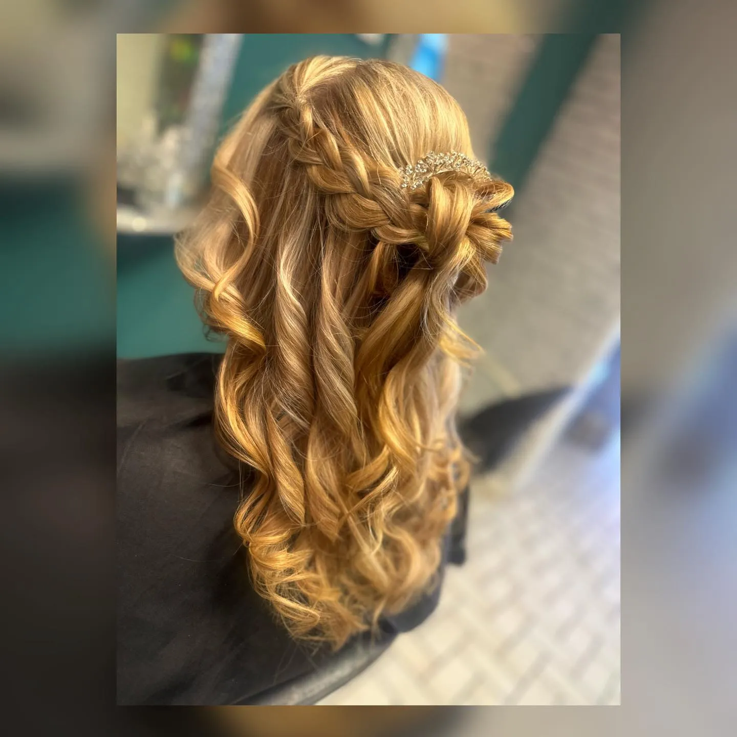 Half-up braided style with curls and crystal hair accessory for a wedding guest